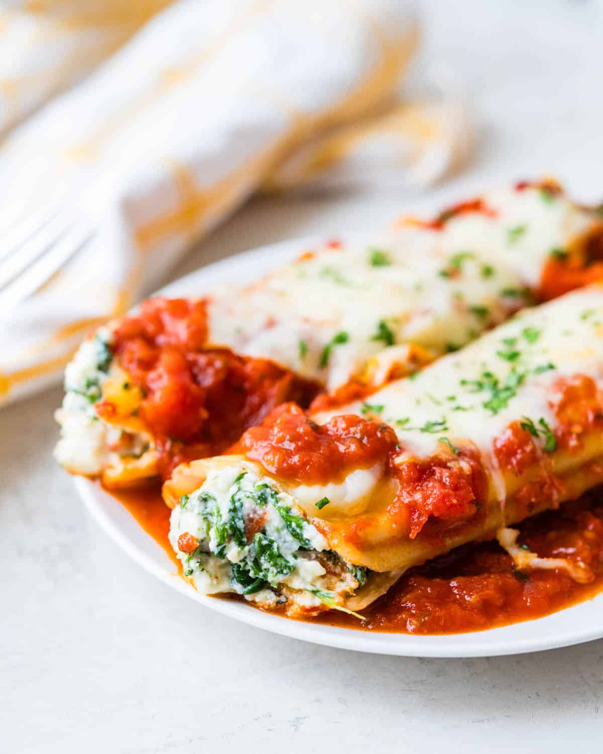 A serving of spinach stuffed manicotti on a white plate.