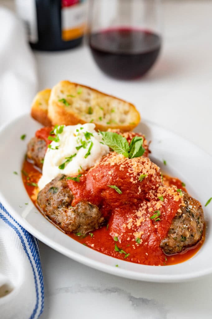 Baked meatballs on a plate with tomato sauce, parmigiano reggiano, ricotta and garlic bread.