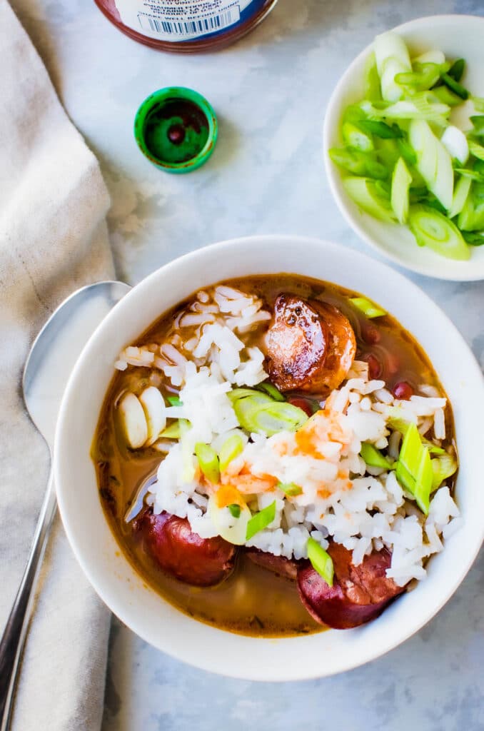 a bowl of red bean soup with rice and hot sauce.