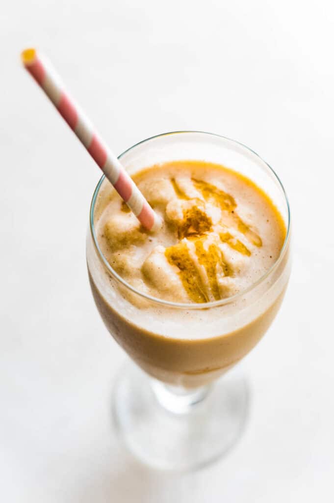 Serving peanut butter banana shake in a glass with a straw and honey garnish.