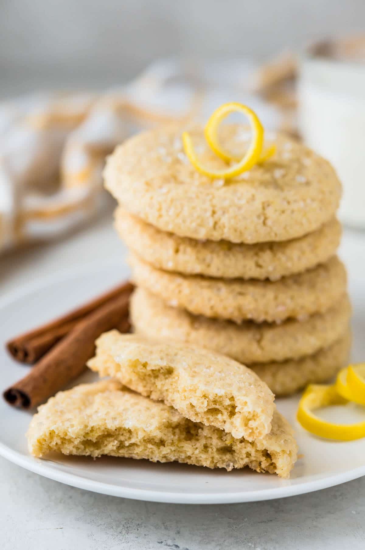 chewy lemon sugar cookies on a plate with a twist of lemon and cinnamon sticks.