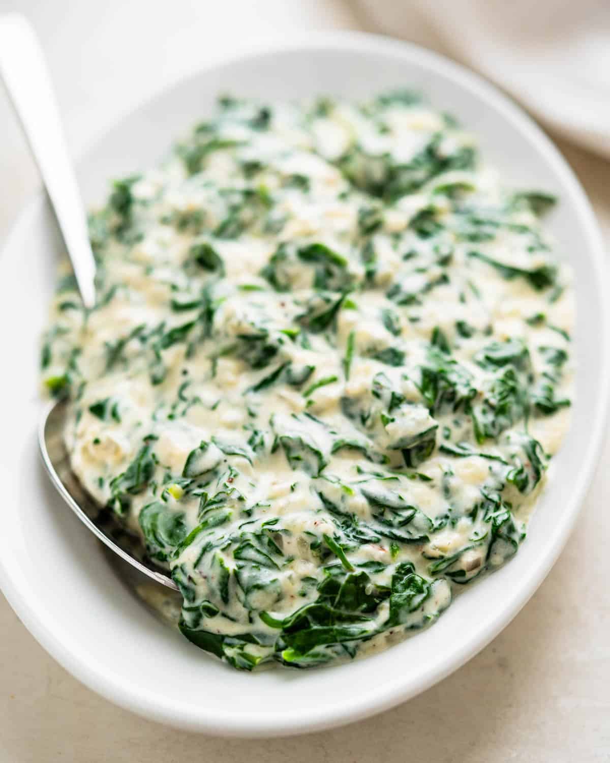 A serving dish of creamed spinach with Boursin cheese and a spoon for scooping.