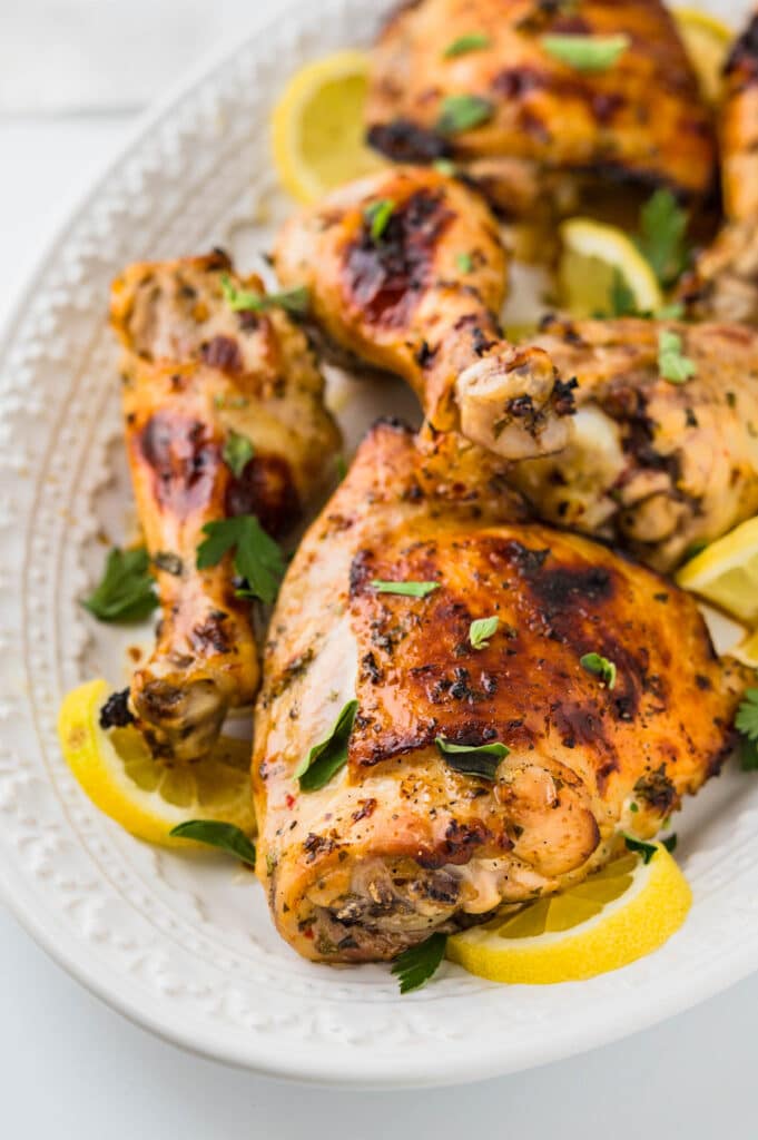 Lemon garlic chicken served on a platter with lemon slices and fresh oregano and herbs.