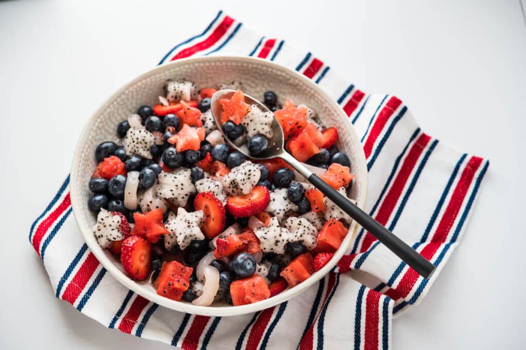serving the red white and blue fruit salad in a bowl.