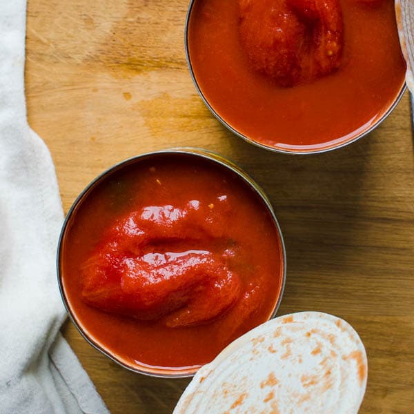 Two cans of San Marzano tomatoes open on a wooden counter.