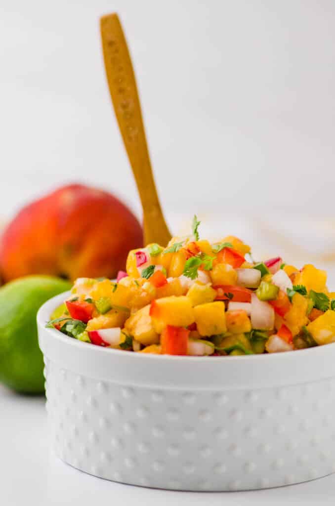 a bowl of peach salsa with a wooden spoon to serve.