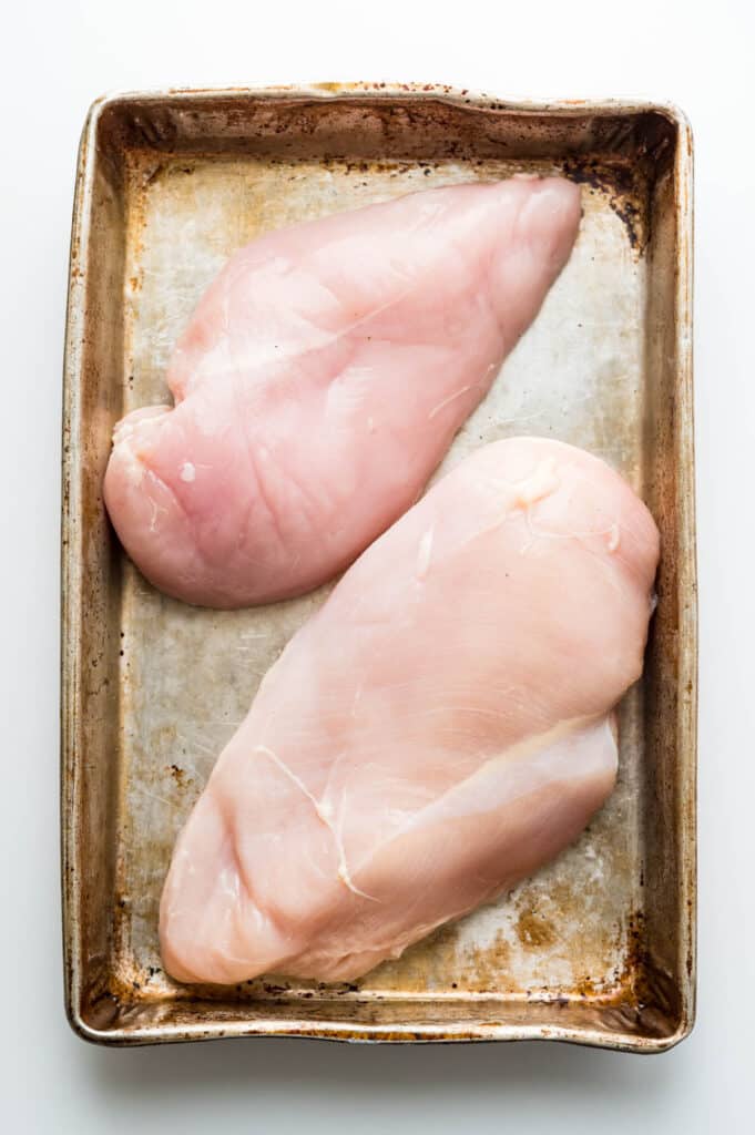 two large boneless skinless chicken breasts on a rimmed baking sheet.