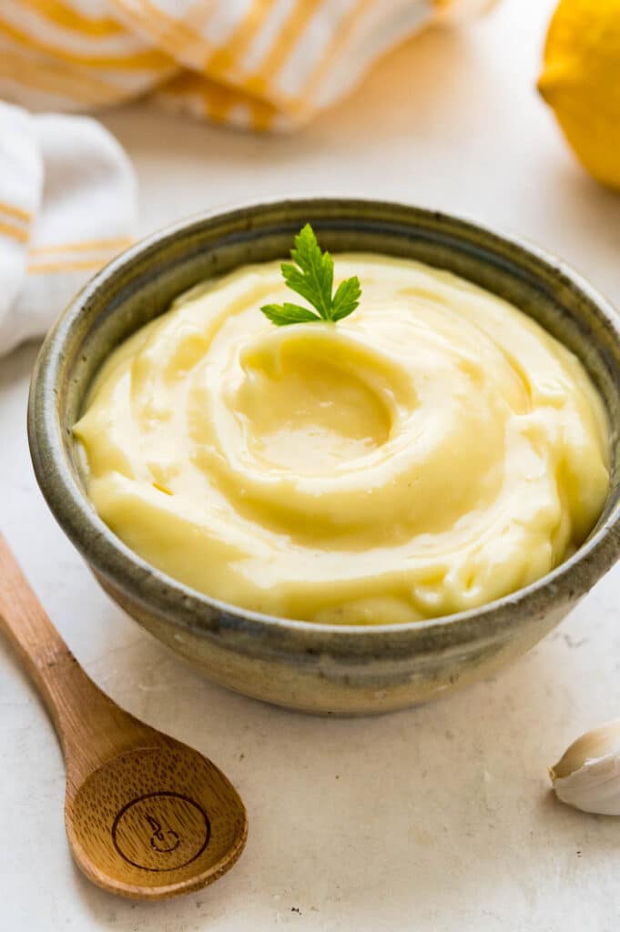 A ceramic bowl filled with aioli sauce and a wooden spoon ready to scoop.