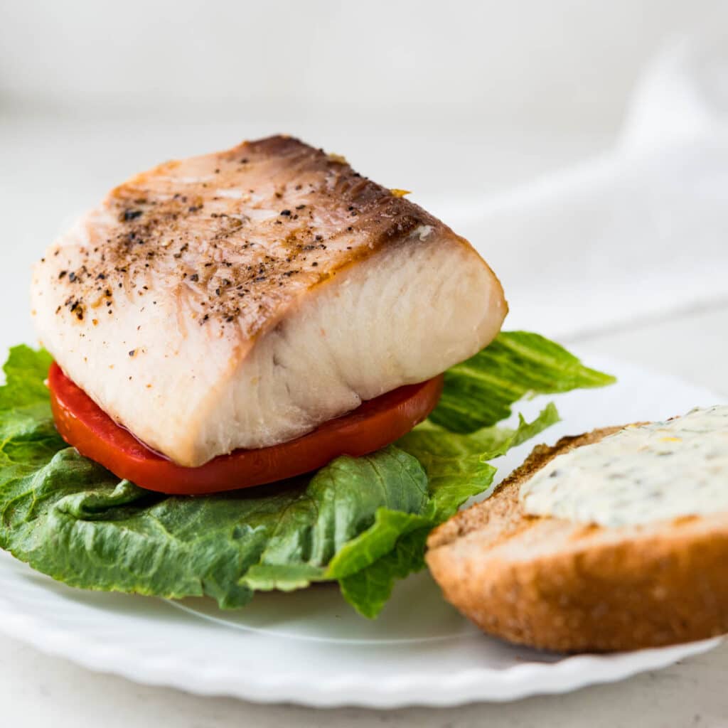 topping the lettuce and tomato with a piece of grilled fish for sandwiches.