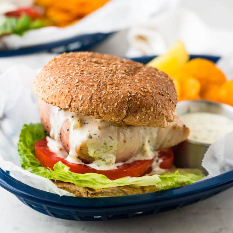 A grilled fish sandwich loaded with lettuce, tomato and tartar sauce on a whole wheat bun.