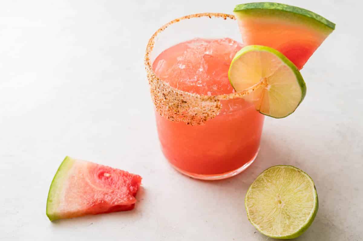 a watermelon margarita on ice with lime and fresh fruit garnish.