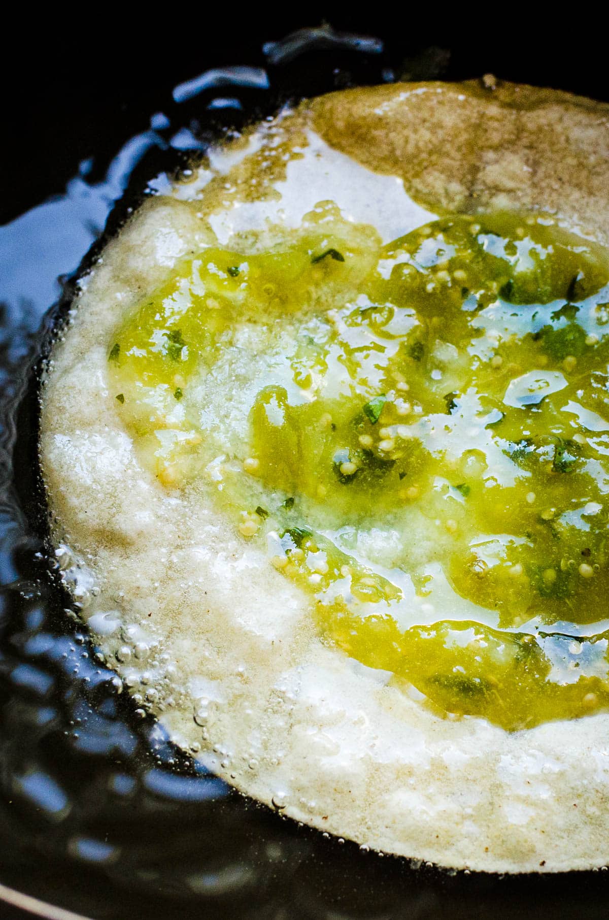 spooning salsa verde onto the corn tortilla while it's frying in the oil to make chalupas.