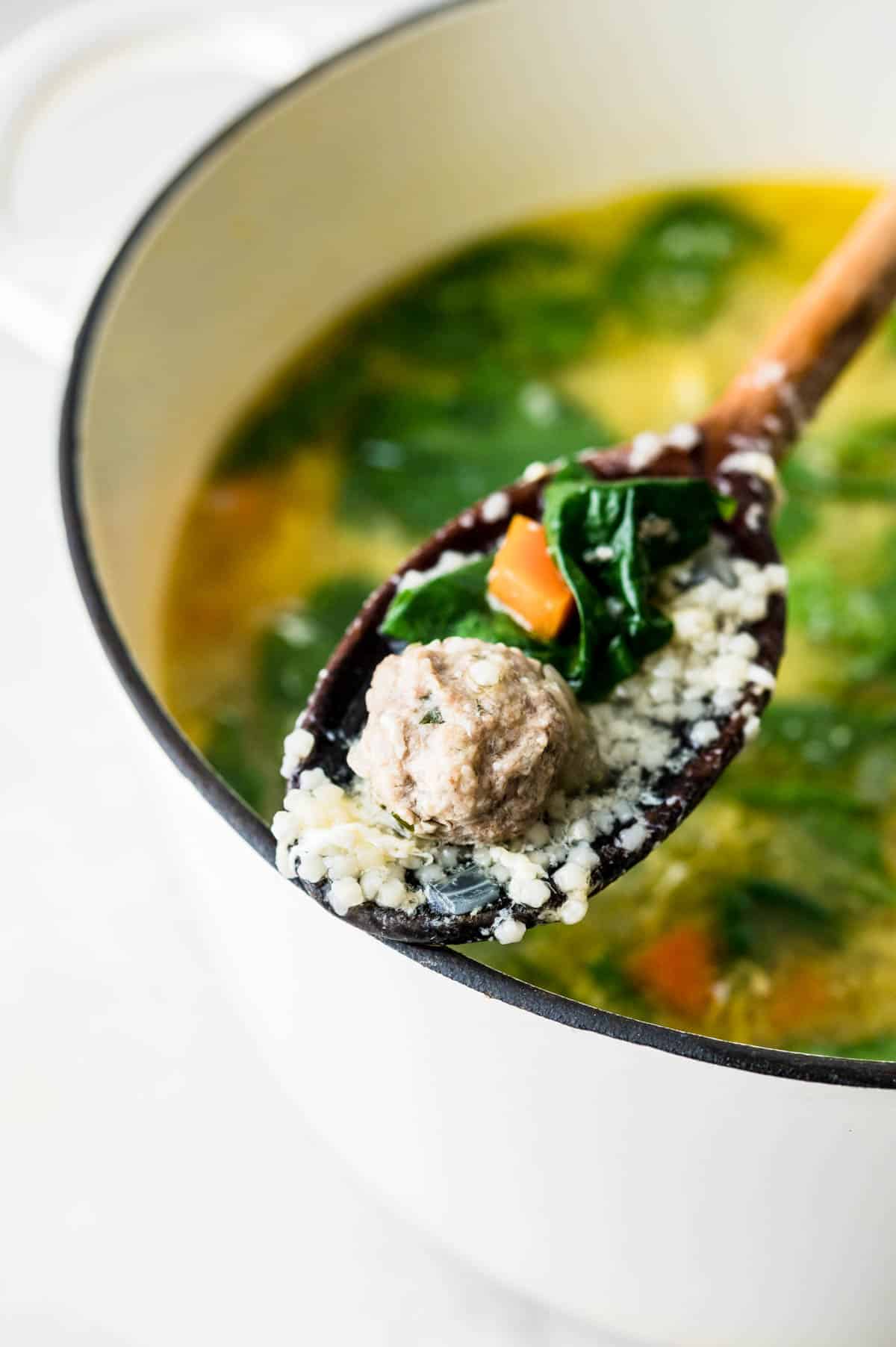 Spooning up a bit of Italian wedding soup recipe on a wooden spoon.