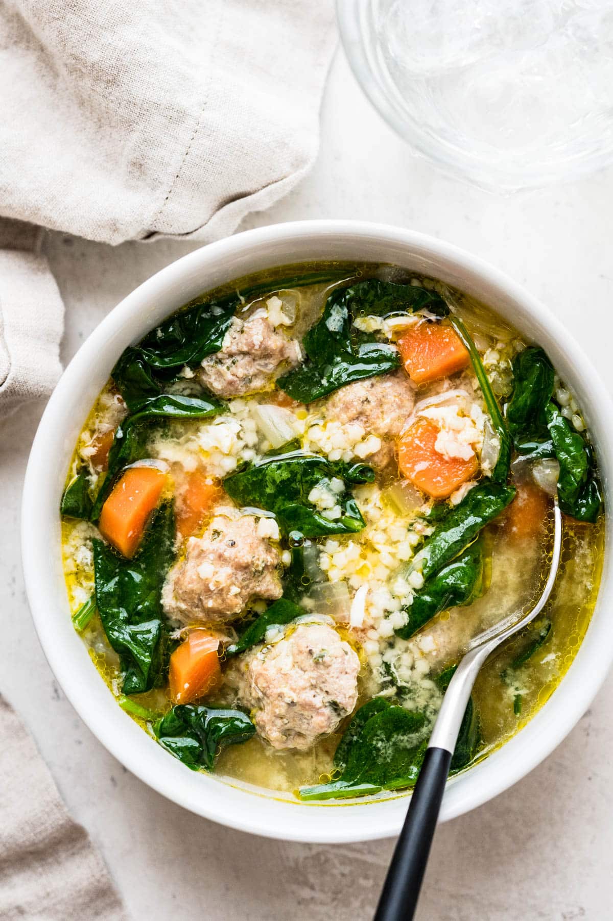 an overhead picture of a bowl of wedding soup with carrots, spinach, meatballs and pasta.