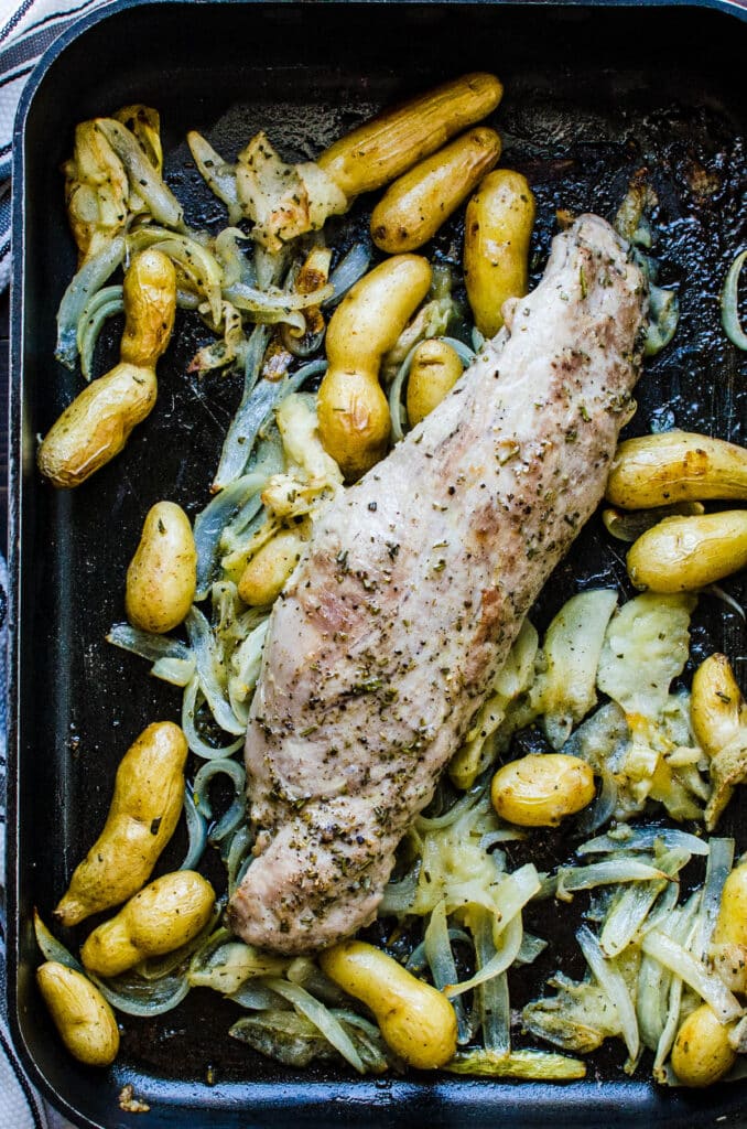 the roasted pork and vegetables resting in a roasting pan.