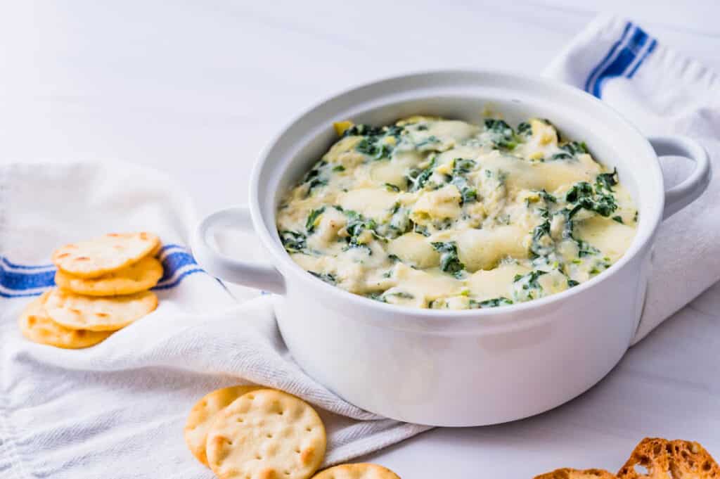 a casserole of baked spinach artichoke dip with crackers and crostini.