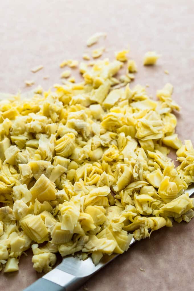 chopping drained and dried artichoke hearts on a cutting board. 