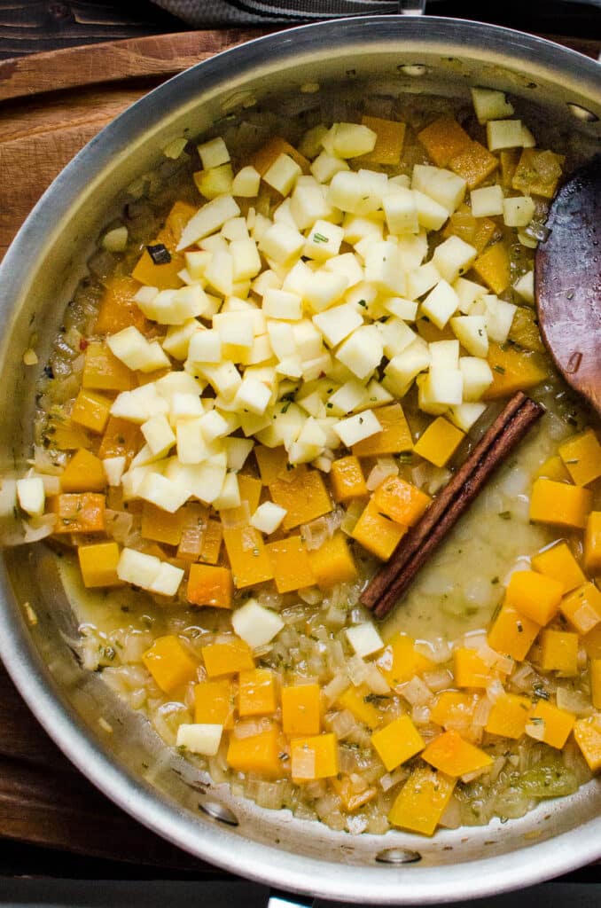 adding diced apples, vegetable broth and a cinnamon stick to the butternut squash.