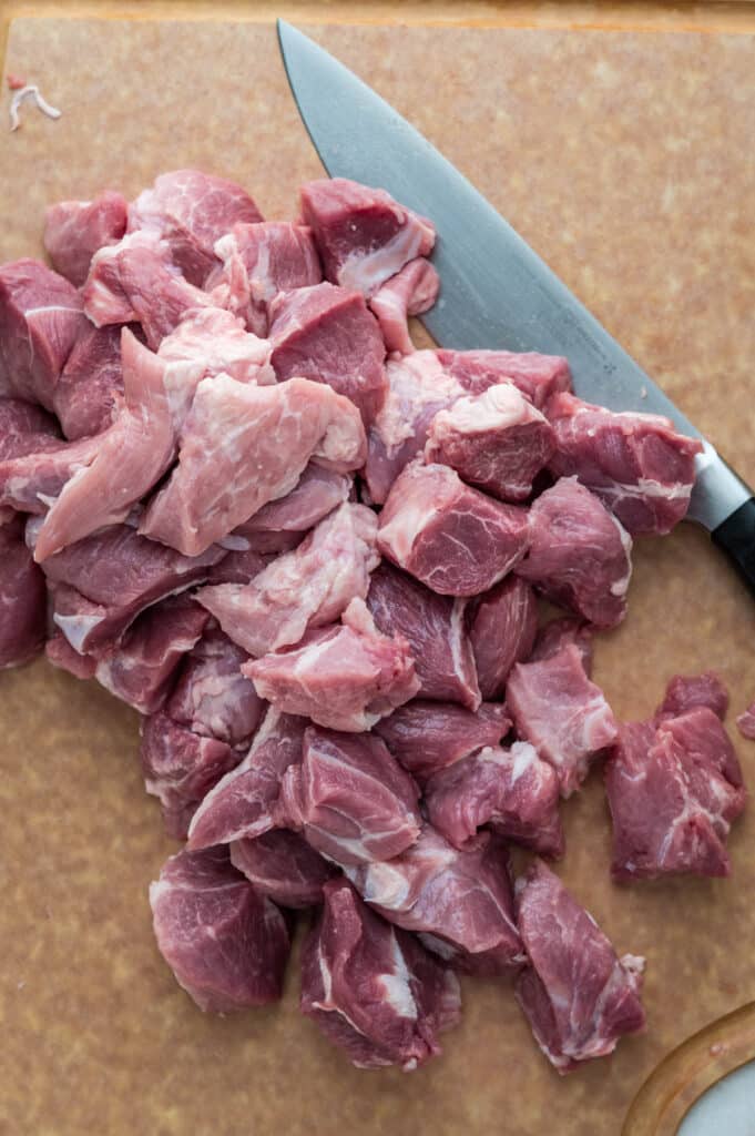 cutting pork shoulder into chunks on a cutting board. 