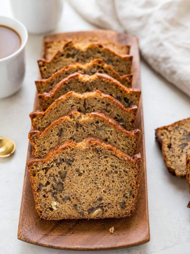 a tray of sliced moist banana bread with pecans and two cups of coffee.