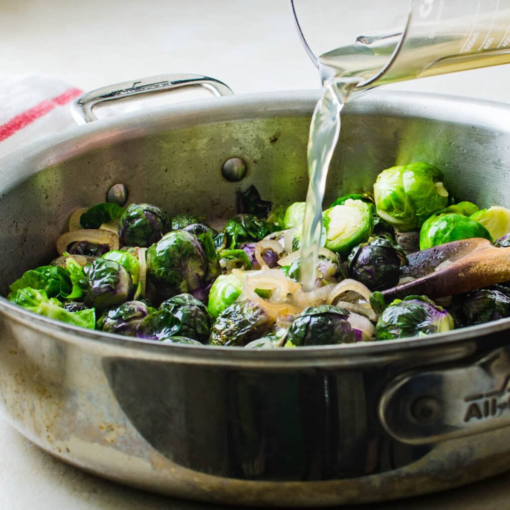 adding broth to the brussels sprouts to braise them.