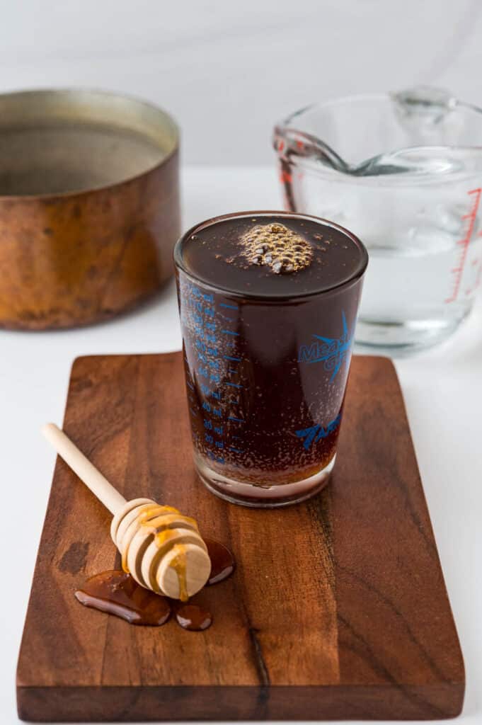 a half cup of honey in a measuring cup with a honey dipper, cup of water and copper pot.