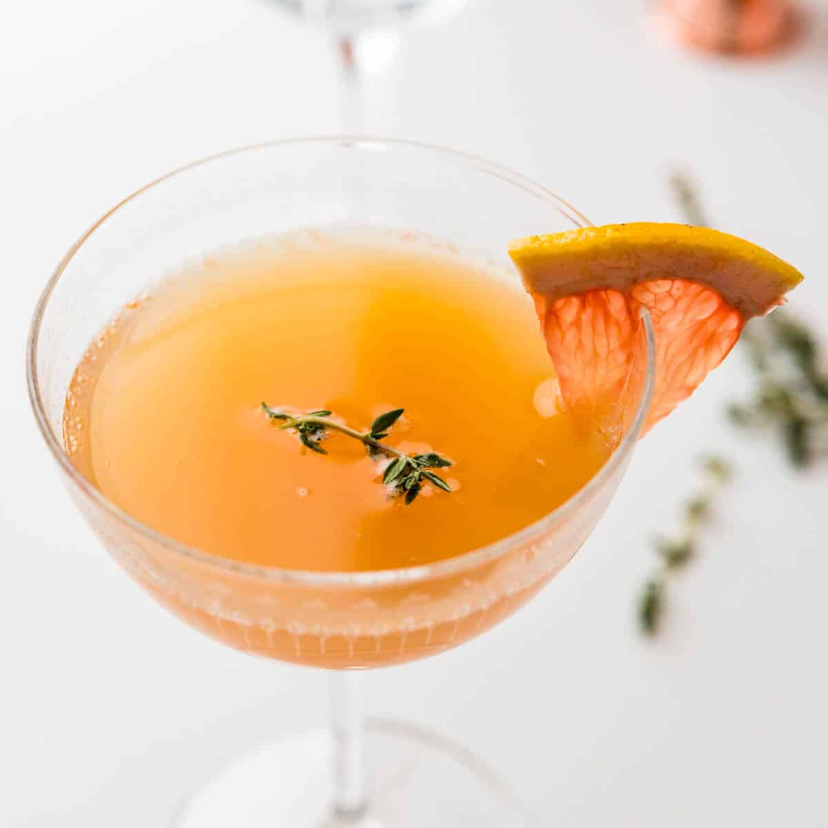 grapefruit juice cocktails in a coupe glass with a wedge of fruit for garnish.