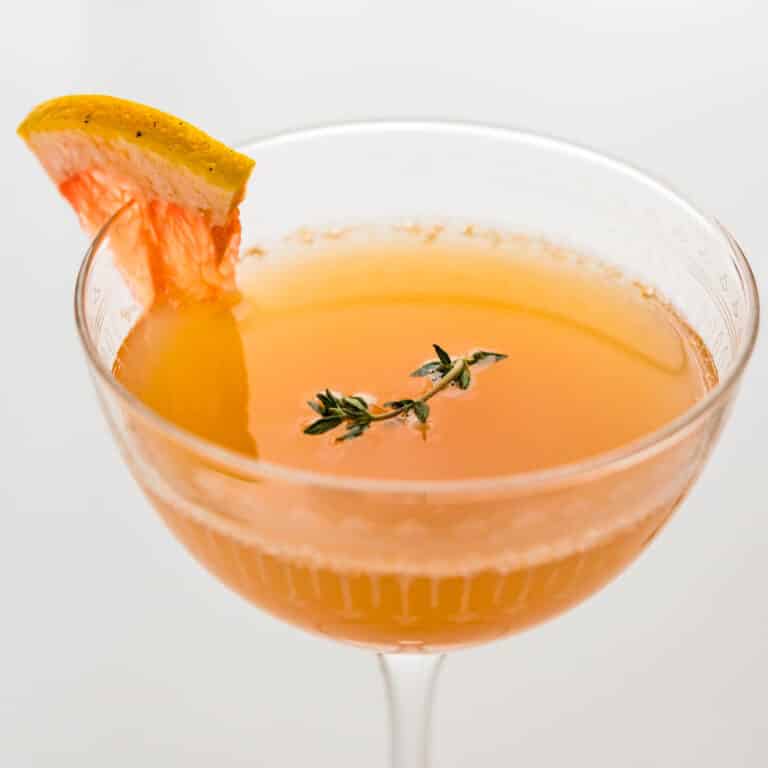 grapefruit mimosa in a coupe glass with thyme garnish.