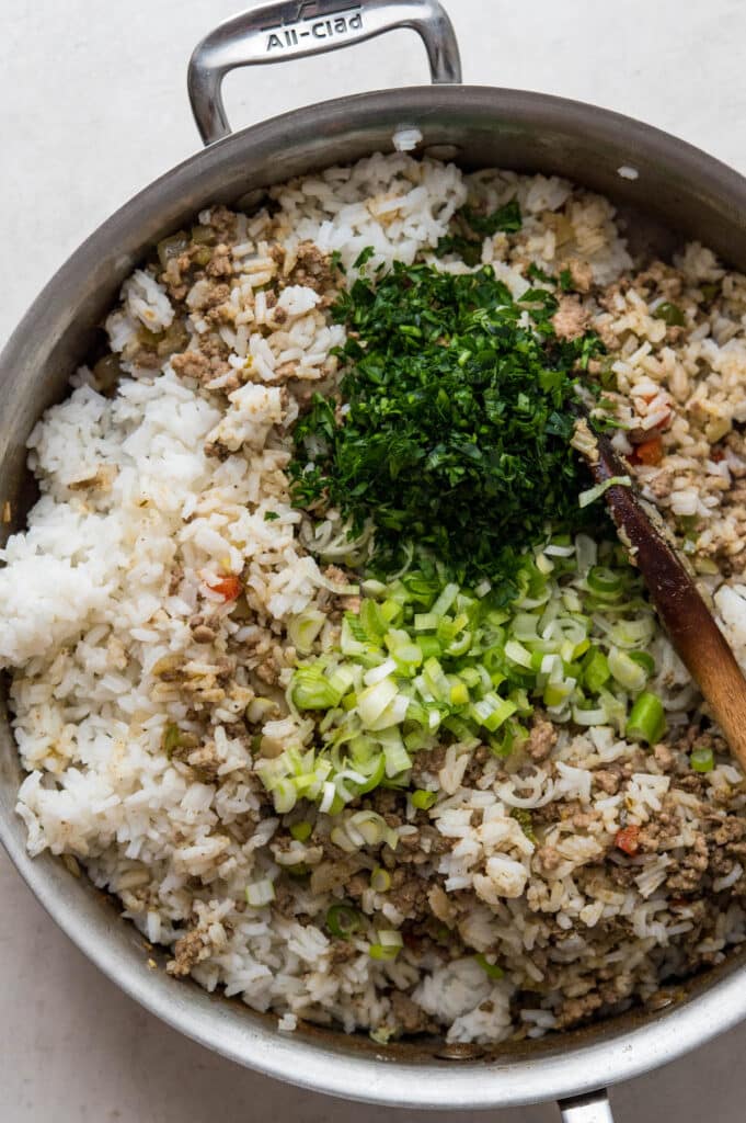 adding green onions and parsley to the rice dressing in a skillet.