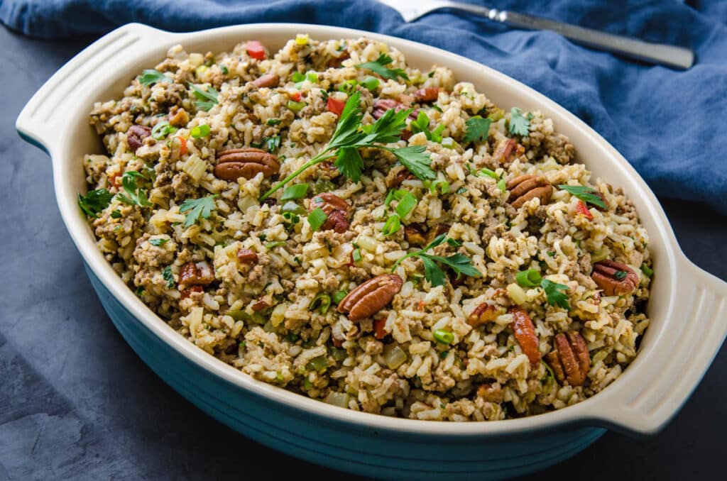 a casserole dish filled with rice dressing and topped with pecans and parsley.