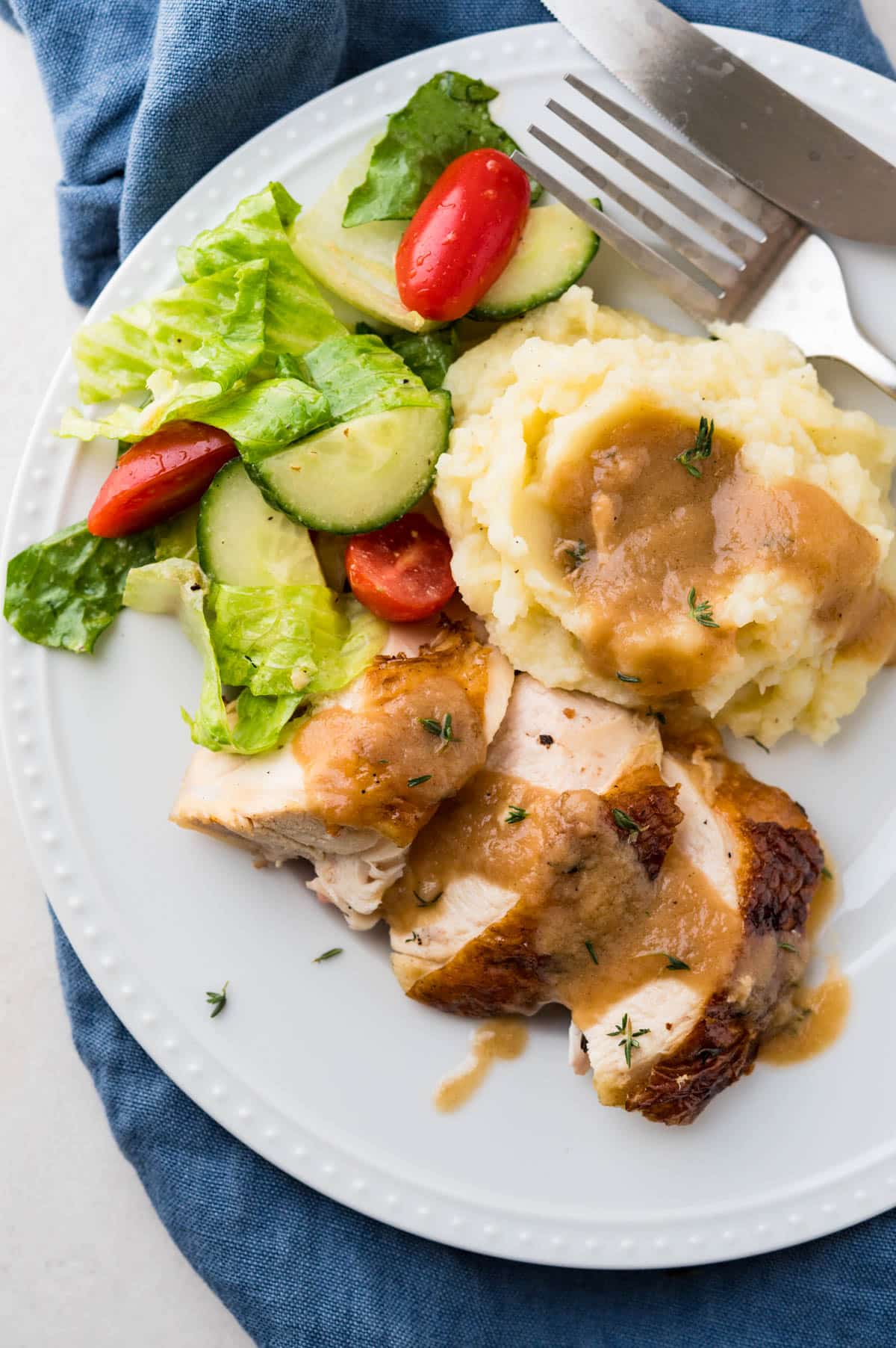 A white plate serving grilled chicken, mashed potatoes and gravy with a green salad.