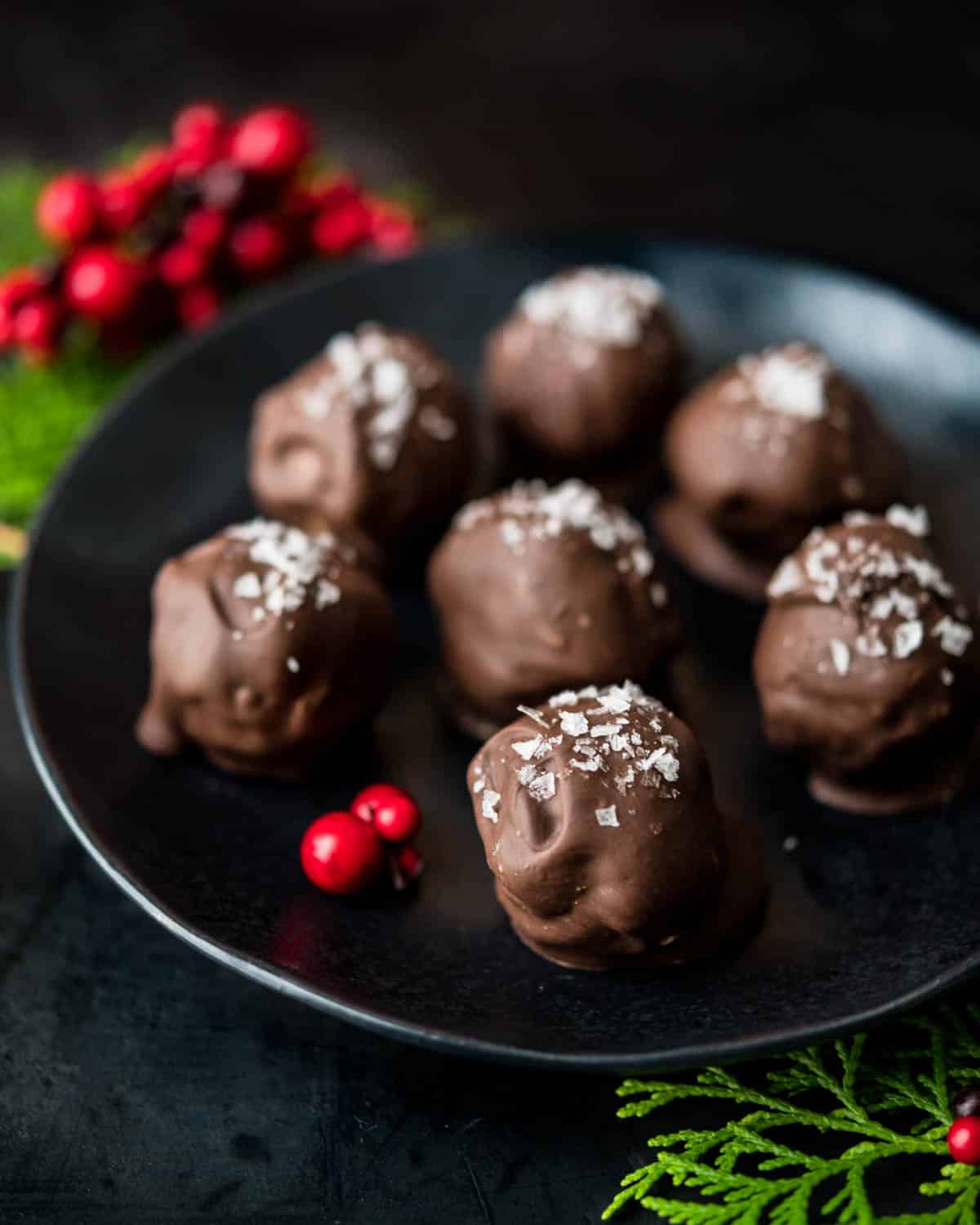 peanut butter chocolate balls on a black plate with holiday greenery and berries.