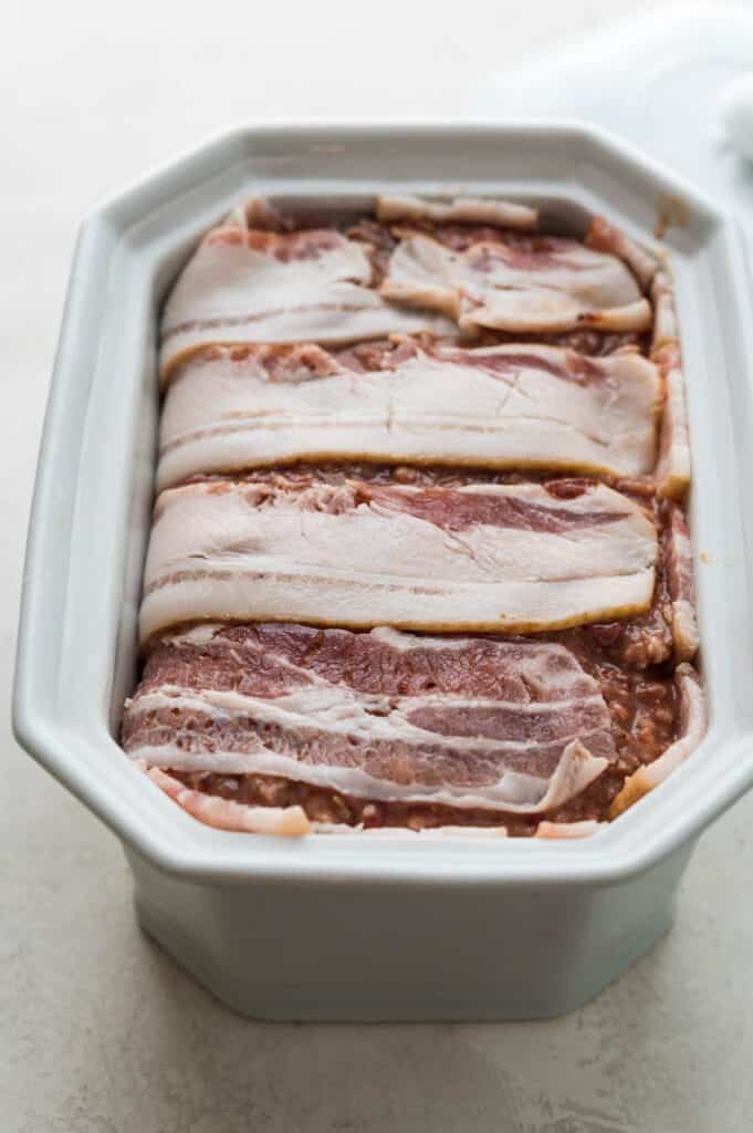 Covering the top of the French pate with bacon to cook in a water bath. 