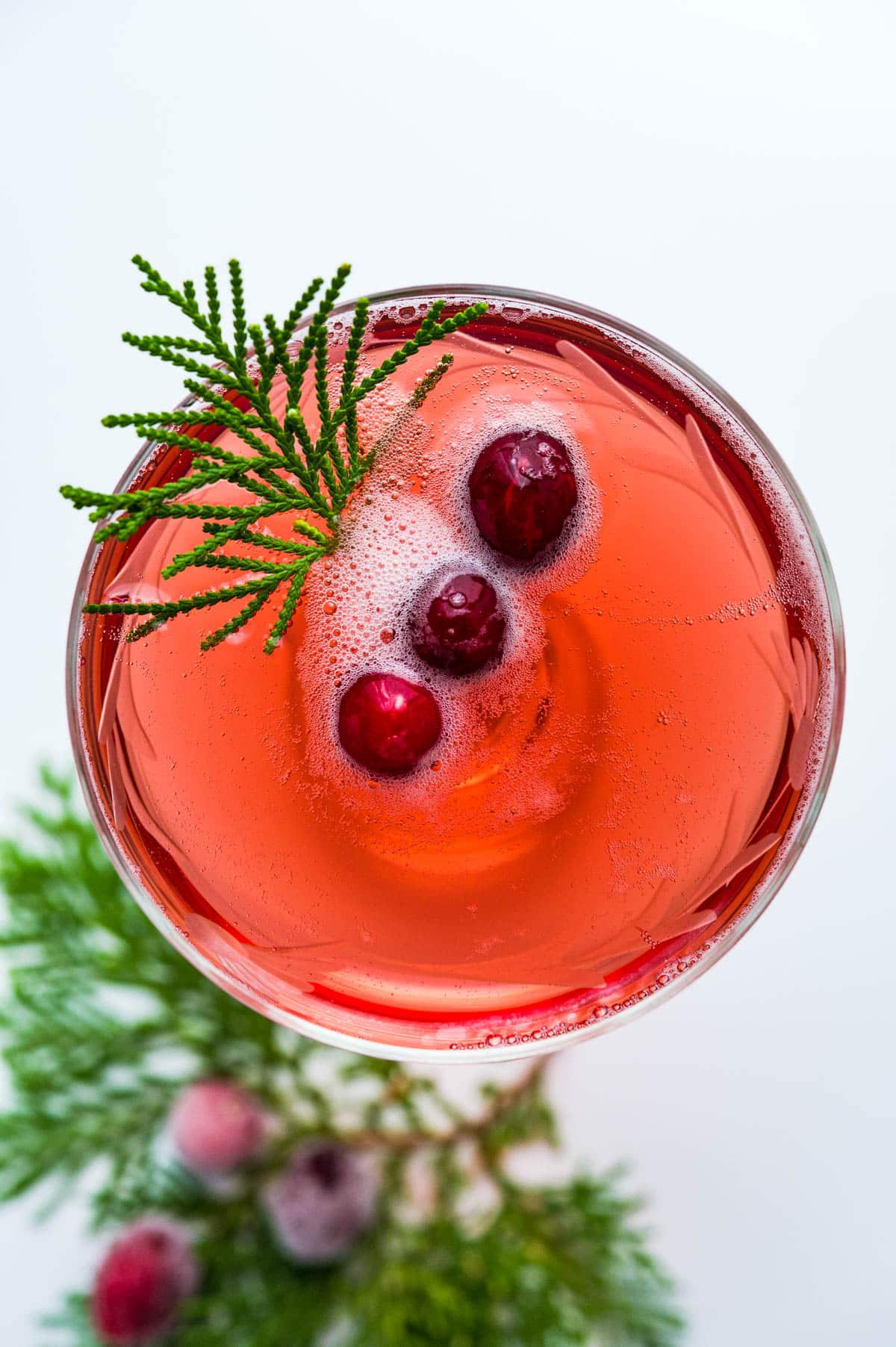 an overhead photo of the cranberry mimosa in a glass with cranberry garnish and sprig of greenery.
