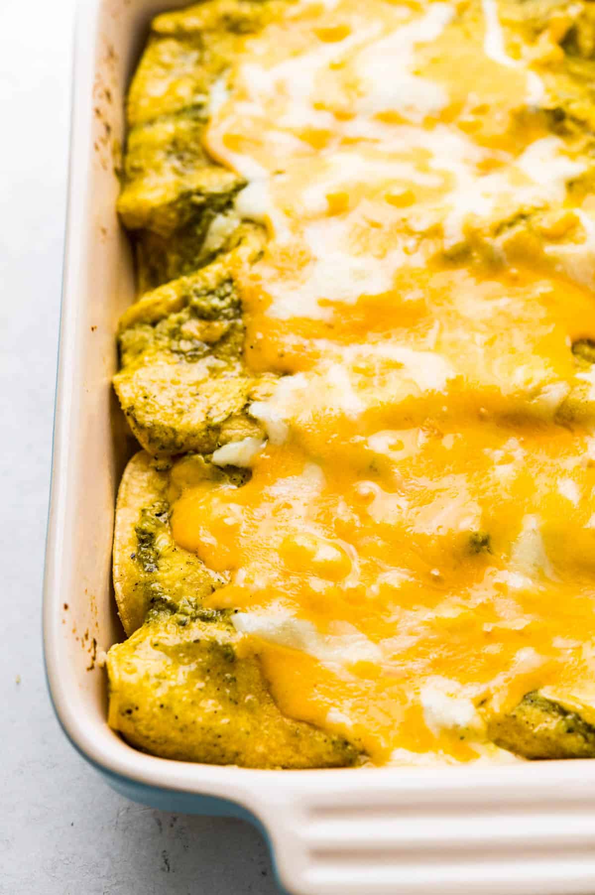 A closeup of the just baked green enchiladas with a lake of cheese melted on top.