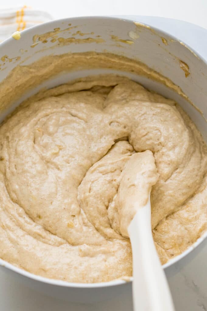 A bowl of thick banana cake batter with a spatula.