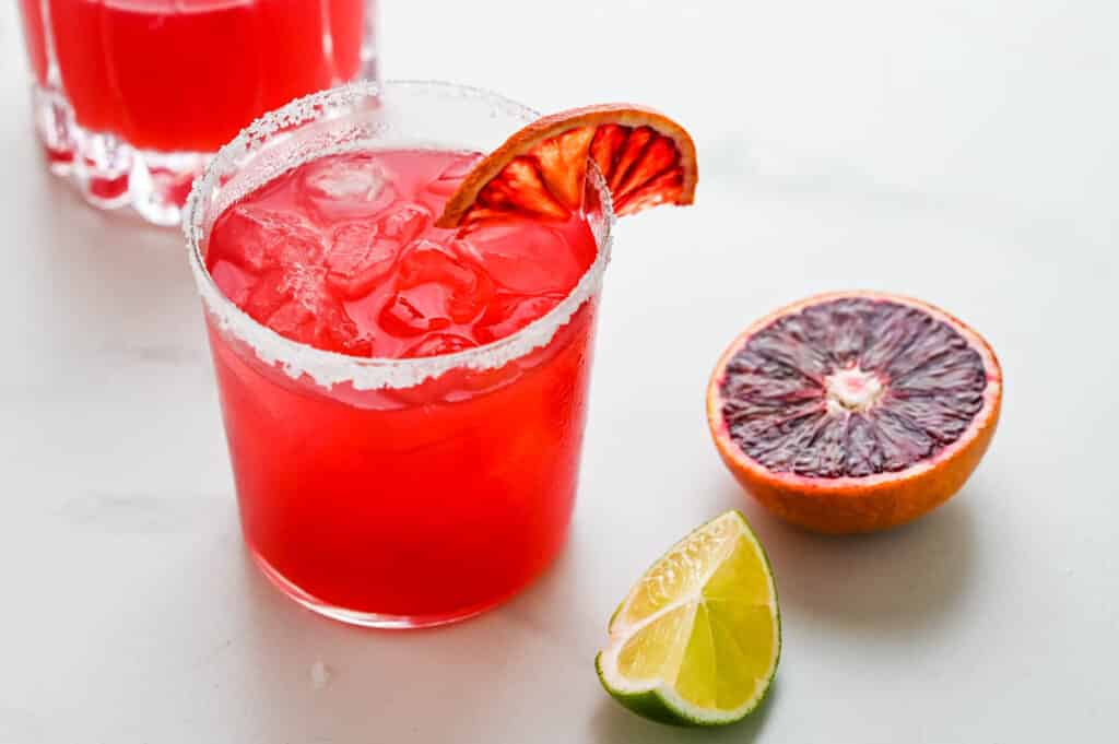 A refreshing glass of red margaritas with a slice of lime and blood orange.