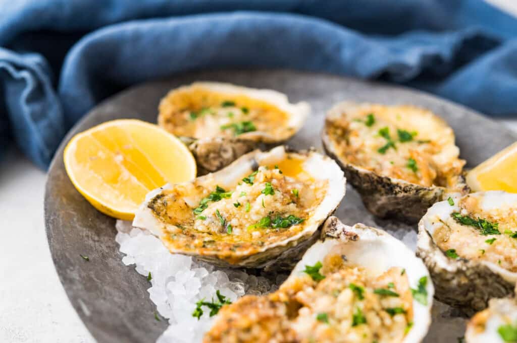 A pewter platter lined with rock salt and topped with chargrilled oysters with lemon wedges.