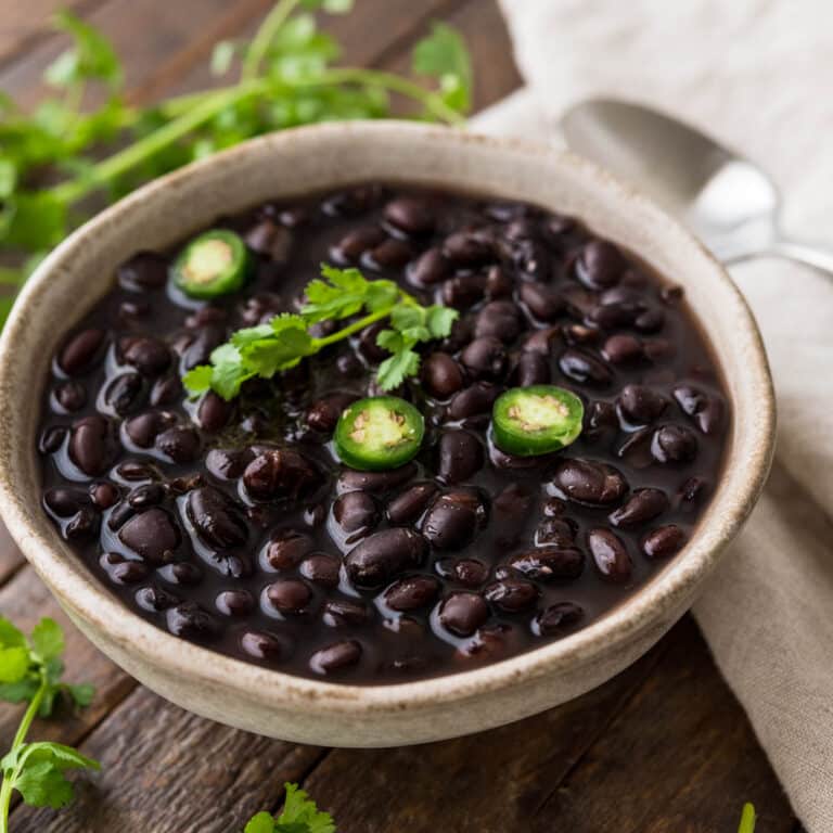 a stone ware bowl of cooked black beans with fresh cilantro and serrano chiles.