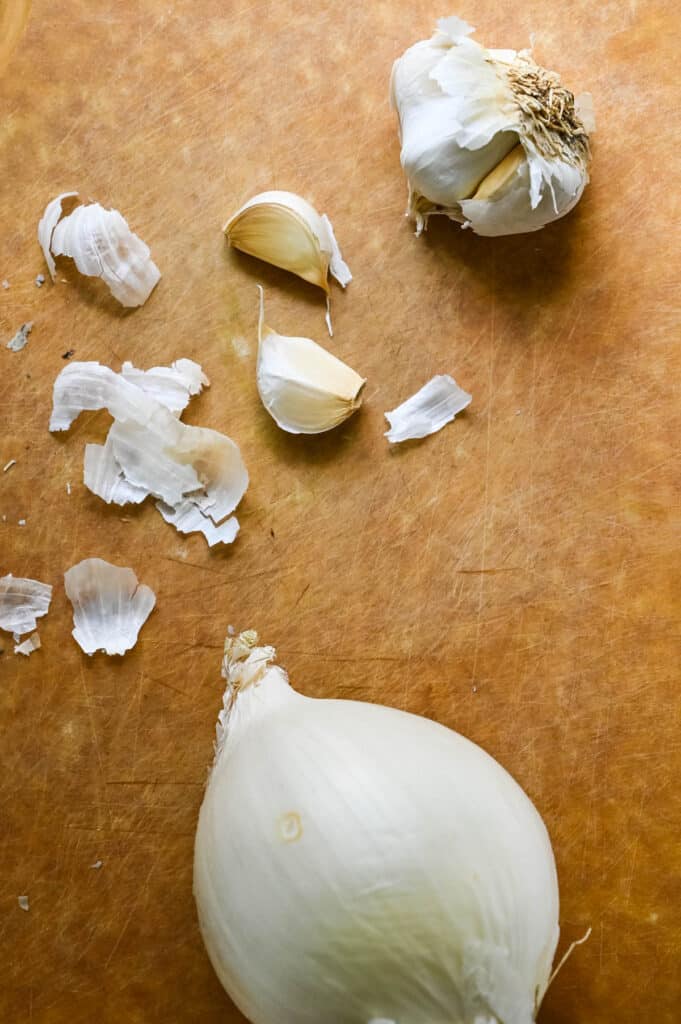 white onions and cloves of garlic on a cutting board. 