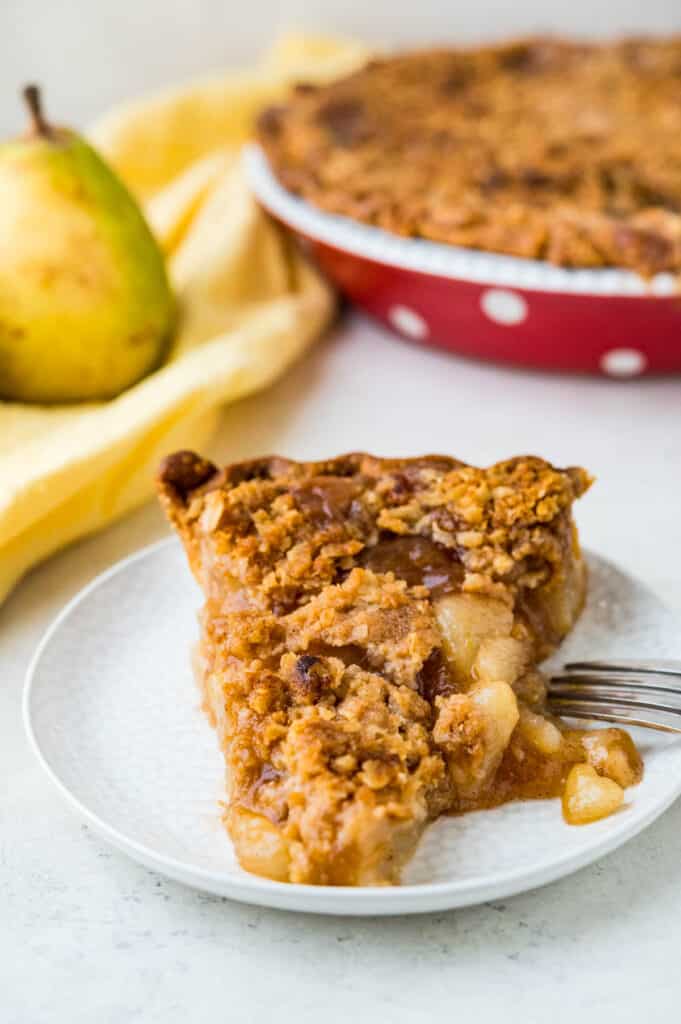 A slice of pear pie with cinnamon oatmeal crumble on a plate. 