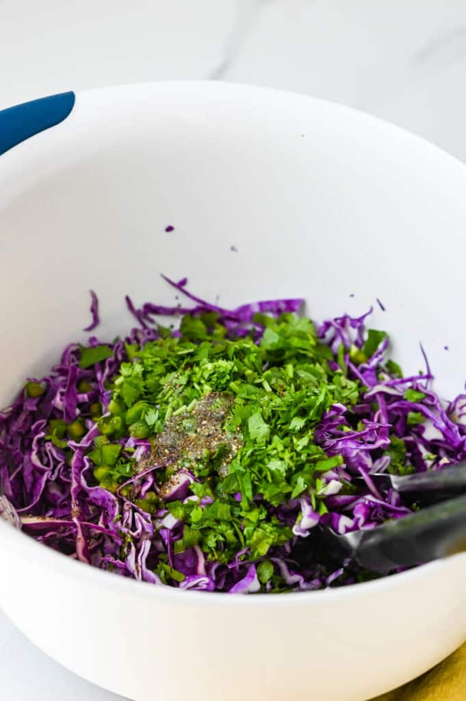 a bowl filled with sliced purple cabbage, jalapenos and cilantro with no mayo slaw dressing.