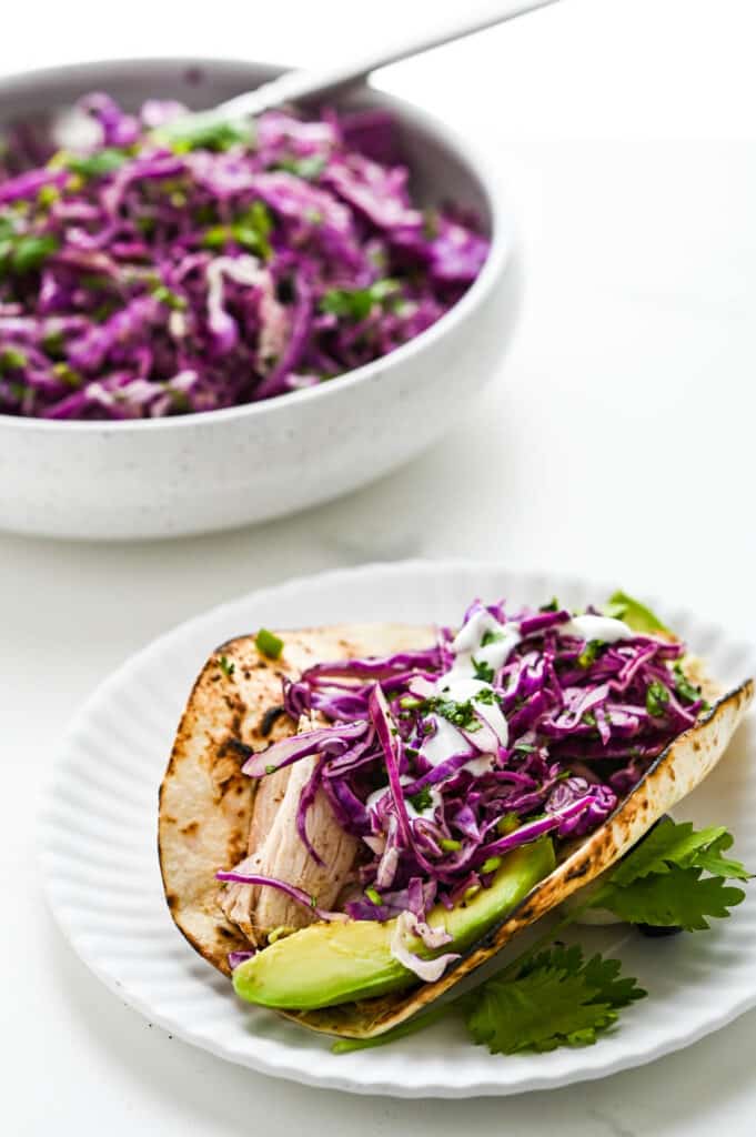 A chicken taco with avocado and crema topped with a generous serving of red cabbage coleslaw.