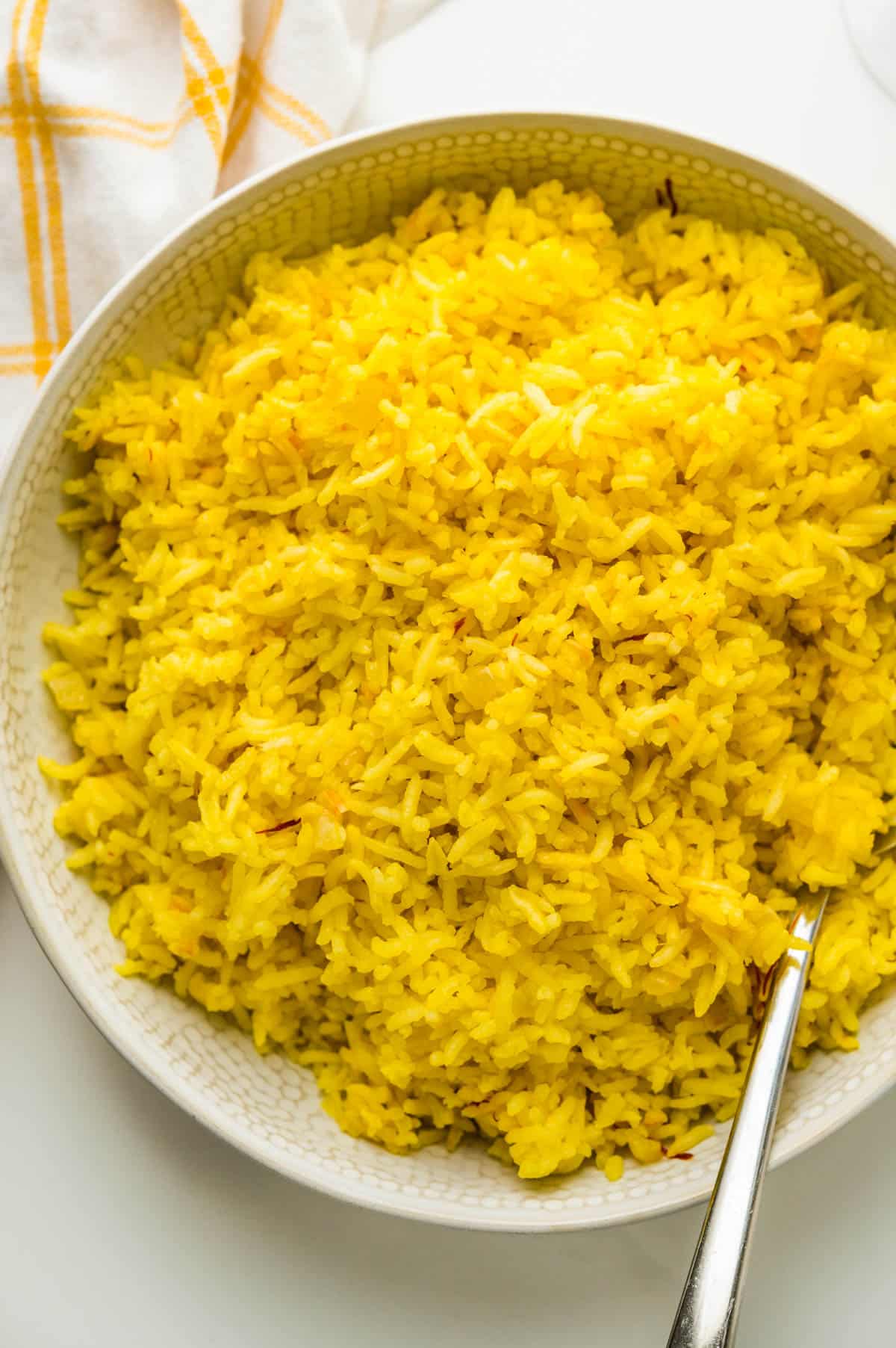 A batch of golden yellow saffron rice recipe in a white bowl with a spoon.