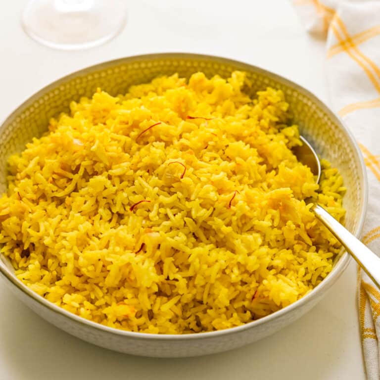 a white bowl filled with saffron rice and a spoon.