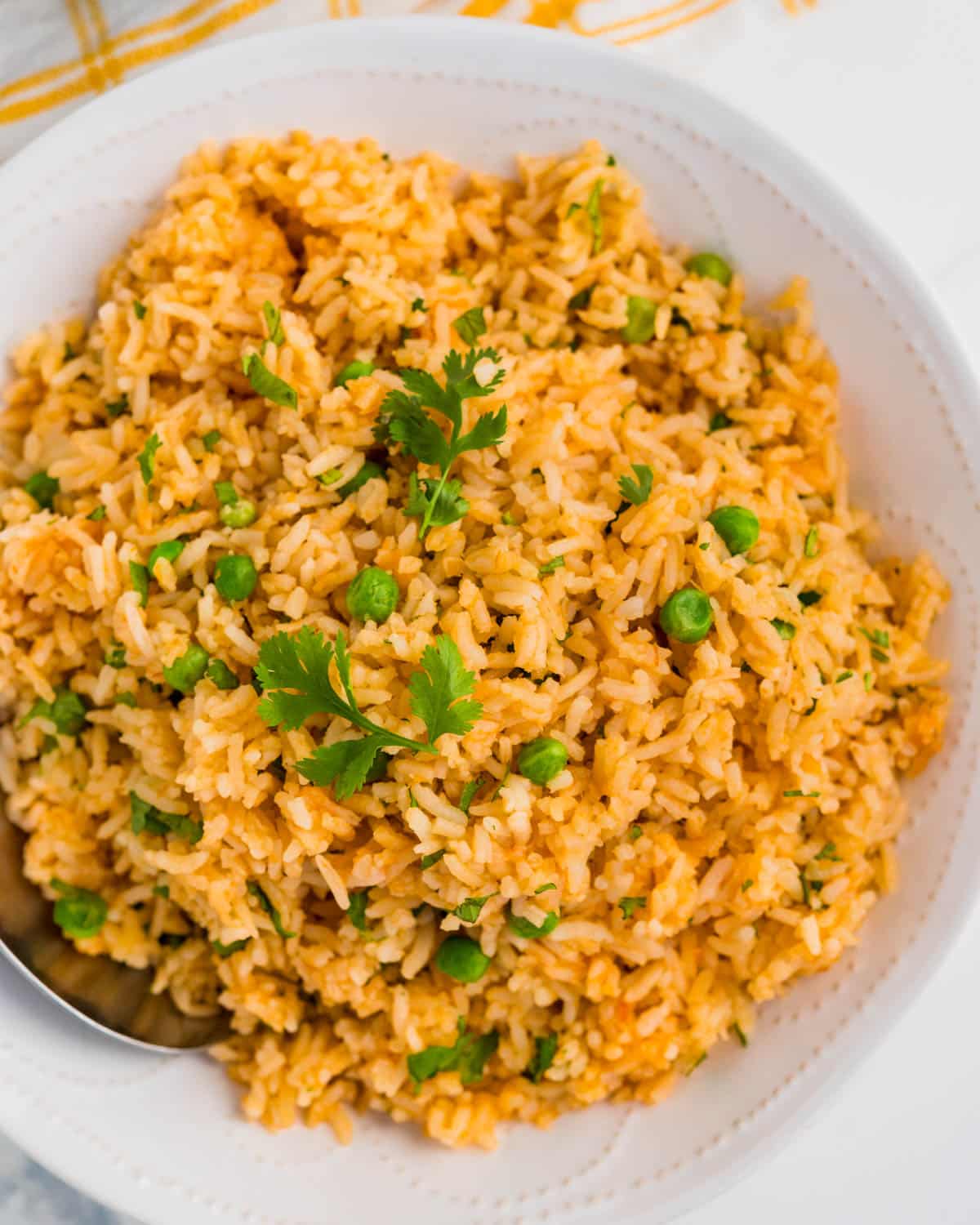 A white bowl filled with arroz roja, cilantro and peas as a side dish.