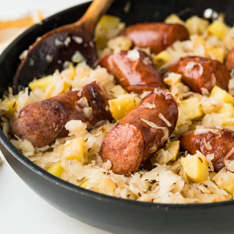 kielbasa and sauerkraut in a skillet with a wooden spoon.
