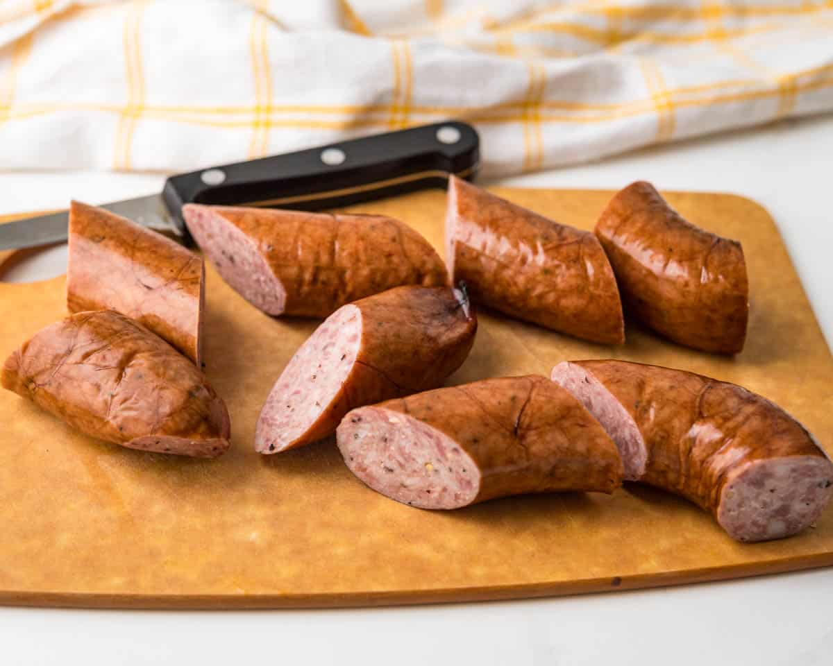 Cutting a ring of smoked kielbasa into two-inch chunks on a wooden board.