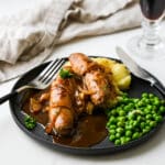 Bangers and Mash with green peas on a black plate with a stout glass.