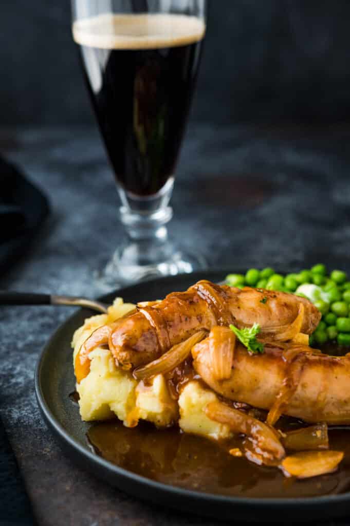 A plate of Irish Bangers and mash with green peas and a pint of Guinness.